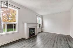 Living area featuring a fireplace with a white mantel, wood-finish flooring, white baseboards, and crown molding - 