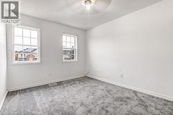 Bright room featuring two double-hung windows, light gray carpeting, crisp white walls, white baseboards, and a ceiling fan with integrated lighting - 