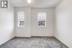 Bright interior room featuring two double-hung windows with grid patterns, plush gray carpeting, white painted walls, and white baseboards - 