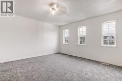 Room featuring a ceiling fan, three double-hung windows, light gray wall-to-wall carpeting, white baseboards, and white painted walls - 