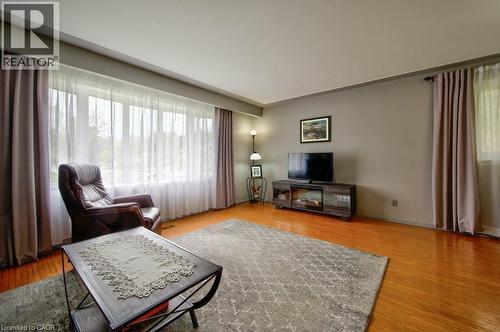 Living area featuring a large window with sheer and blackout curtains, warm-toned wood-finish flooring, and light gray walls - 34 Westwood Crescent, Kitchener, ON - Indoor Photo Showing Living Room