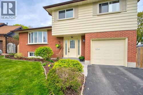 Split-level residence featuring a brick and siding exterior, an integrated garage, a bay window, and a well-maintained lawn with landscaping - 34 Westwood Crescent, Kitchener, ON - Outdoor With Exterior
