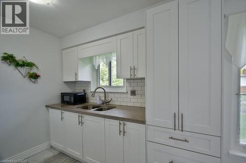 Kitchen featuring white shaker-style cabinetry, a double basin stainless steel sink with a gooseneck faucet, light-toned countertop, and white subway tile backsplash - 34 Westwood Crescent, Kitchener, ON - Indoor Photo Showing Kitchen With Double Sink