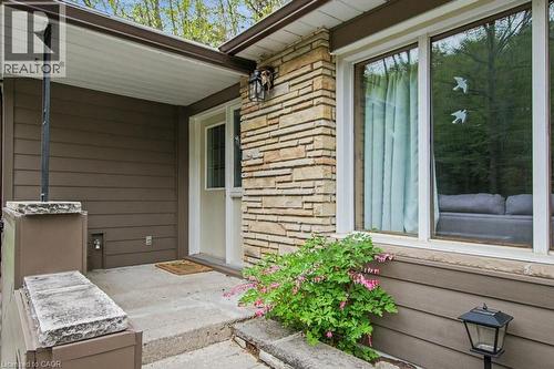 Entryway featuring stacked stone facade, brown horizontal siding, a covered porch, a white entry door, and large picture windows - 1333 Hidden Valley Road, Burlington, ON - Outdoor With Exterior