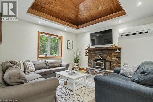 Living area featuring a tray ceiling with wood-finish paneling, a stone-front fireplace with a wood mantel, a large window with wood trim, and recessed lighting - 1333 Hidden Valley Road, Burlington, ON - Indoor Photo Showing Living Room With Fireplace