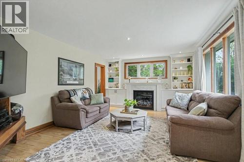 Living area featuring a fireplace with a stone surround, built-in shelving, wood-finish flooring, and large windows - 1333 Hidden Valley Road, Burlington, ON - Indoor Photo Showing Living Room With Fireplace