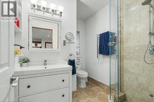 Bathroom featuring a white vanity with integrated sink, chrome faucet, wall-mounted mirror, and a glass-enclosed shower with natural stone-look tiling - 1333 Hidden Valley Road, Burlington, ON - Indoor Photo Showing Bathroom