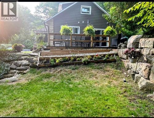 Rear exterior featuring a spacious wooden deck with railings, stone retaining walls, terraced gardens, and sliding glass doors - 1333 Hidden Valley Road, Burlington, ON - Outdoor With Deck Patio Veranda