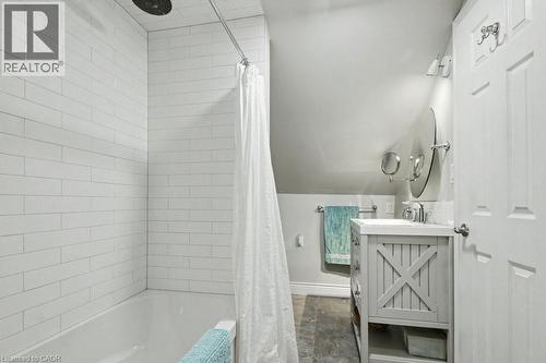 Bathroom featuring a white subway tile shower surround, a built-in tub, a light gray vanity with X-panel detailing, a circular mirror, and wall-mounted lighting - 1333 Hidden Valley Road, Burlington, ON - Indoor Photo Showing Bathroom