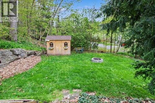 Expansive grassy yard featuring a wood-sided shed with arched windows and a stone retaining wall - 1333 Hidden Valley Road, Burlington, ON - Outdoor