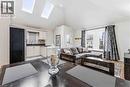 Open-concept living area featuring a vaulted ceiling with two skylights, a kitchen with light-toned cabinetry and a tiled backsplash, wood-finish flooring, and a large window with white trim - 74 Province Street N, Hamilton, ON  - Indoor Photo Showing Living Room 