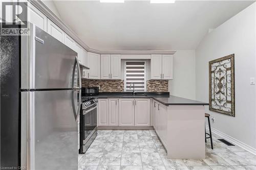 U-shaped kitchen featuring light-toned cabinetry, dark countertops, and a mosaic tile backsplash - 74 Province Street N, Hamilton, ON - Indoor Photo Showing Kitchen With Stainless Steel Kitchen