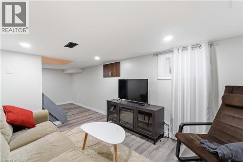 Recessed lighting illuminates this room featuring wood-finish flooring, white walls, and a built-in wall cabinet with wood-tone doors - 74 Province Street N, Hamilton, ON - Indoor Photo Showing Basement