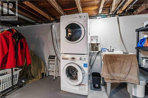 Dedicated laundry area featuring a stacked washer and dryer unit, exposed ceiling joists, and a utility sink - 74 Province Street N, Hamilton, ON - Indoor Photo Showing Laundry Room