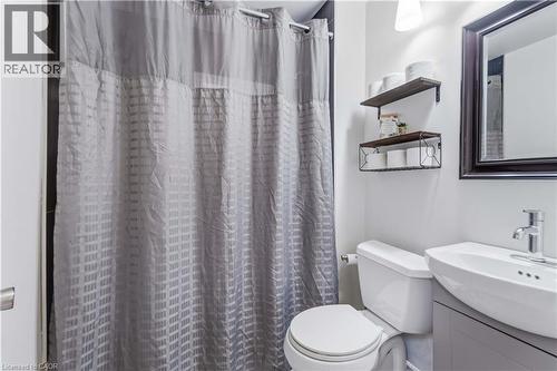 Bathroom featuring a white toilet, wall-mounted shelving, framed mirror, and a vanity with an integrated sink and chrome faucet - 74 Province Street N, Hamilton, ON - Indoor Photo Showing Bathroom