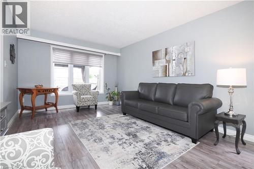 Spacious living area featuring light blue walls, wood-finish flooring, a large window with horizontal blinds, and white trim - 70 Queen Charlotte Crescent, Kitchener, ON - Indoor Photo Showing Living Room