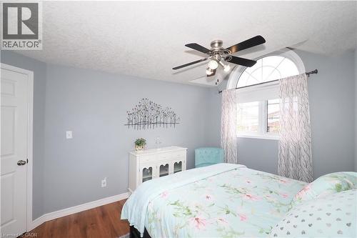 Arched transom window with accompanying rectangular window, wood-finish flooring, ceiling fan with brushed nickel finish, white paneled interior door, and light gray wall paint - 70 Queen Charlotte Crescent, Kitchener, ON - Indoor Photo Showing Bedroom