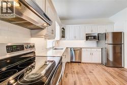 Kitchen featuring white cabinetry, stainless steel appliances, a white subway tile backsplash, light wood-finish flooring, and white countertops - 