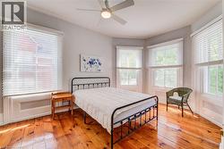Charming bedroom featuring polished hardwood flooring, multiple windows with white blinds, a ceiling fan, and white baseboards - 