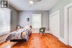 Bedroom featuring warm wood-finish flooring, two windows with white blinds, and a ceiling fan - 