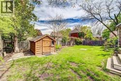 Expansive backyard featuring a manicured lawn, perimeter fencing, mature trees, and a wooden storage shed - 