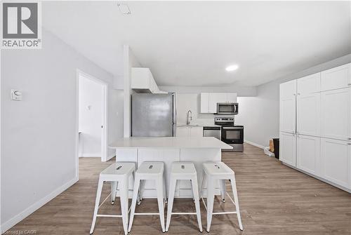 Modern kitchen featuring an island with seating, white shaker-style cabinetry, stainless steel appliances, and wood-finish flooring - 91 Westmount Road Unit# 3, Waterloo, ON - Indoor