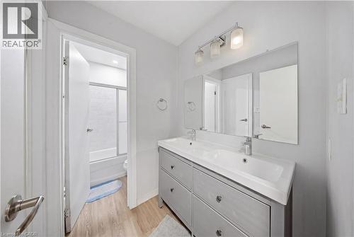 Bathroom featuring a dual-sink vanity with gray cabinetry, a large wall-mounted mirror, and wood-finish flooring - 91 Westmount Road Unit# 3, Waterloo, ON - Indoor Photo Showing Bathroom