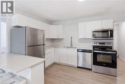 Kitchen featuring white cabinetry, light countertops, wood-finish flooring, stainless steel appliances, and a tiled backsplash - 91 Westmount Road Unit# 3, Waterloo, ON - Indoor Photo Showing Kitchen With Stainless Steel Kitchen