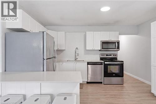 Modern kitchen featuring white cabinetry, light-toned wood-finish flooring, stainless steel appliances, a white tile backsplash, and a breakfast bar - 91 Westmount Road Unit# 3, Waterloo, ON - Indoor Photo Showing Kitchen With Stainless Steel Kitchen