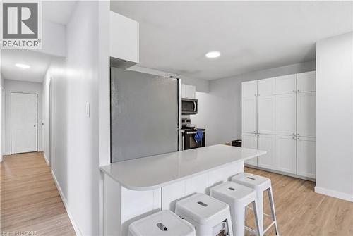 Kitchen featuring a breakfast bar with solid surface countertop, stainless steel refrigerator, built-in microwave, white cabinetry, and wood-finish flooring - 91 Westmount Road Unit# 3, Waterloo, ON - Indoor