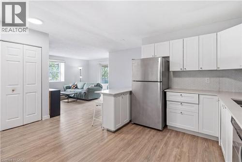 Contemporary kitchen featuring white cabinetry, light-toned wood-finish flooring, and a stainless steel refrigerator - 91 Westmount Road Unit# 3, Waterloo, ON - Indoor Photo Showing Kitchen