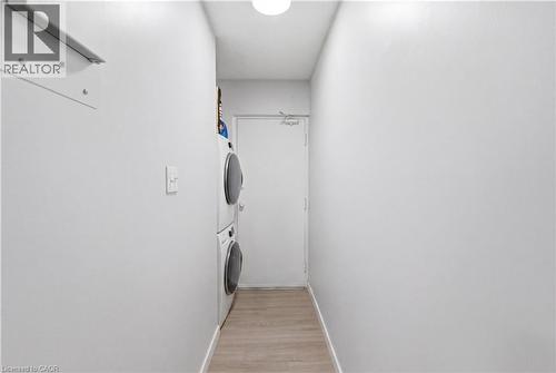 Laundry area featuring stacked appliances, wood-finish flooring, and a white interior door - 91 Westmount Road Unit# 3, Waterloo, ON - Indoor Photo Showing Laundry Room