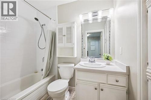 Bathroom featuring a vanity with an integrated sink, a rectangular mirror with integrated lighting, a toilet, a built-in tub with a shower fixture, and white wall tiling - 87 Barbara Crescent, Kitchener, ON - Indoor Photo Showing Bathroom