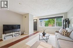 Living area featuring light wood-finish flooring with dark wood-finish accents, recessed ceiling lighting, and a large front window with black blinds - 