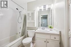 Bathroom featuring a vanity with an integrated sink, a rectangular mirror with integrated lighting, a toilet, a built-in tub with a shower fixture, and white wall tiling - 