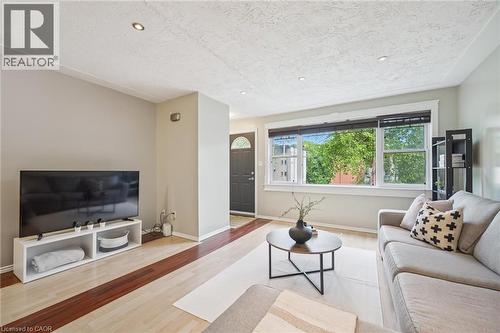 Living area featuring light wood-finish flooring with dark wood-finish accents, recessed ceiling lighting, and a large front window with black blinds - 87 Barbara Crescent, Kitchener, ON - Indoor Photo Showing Living Room