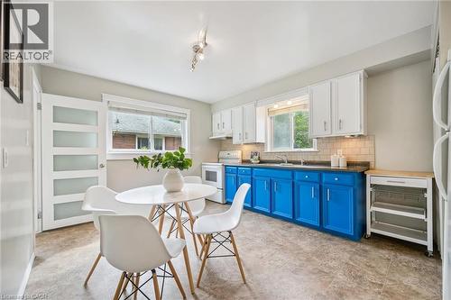 Bright kitchen featuring white upper cabinetry, vibrant blue lower cabinetry, a light-toned tile backsplash, and a window above the sink - 87 Barbara Crescent, Kitchener, ON - Indoor