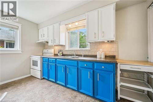 Kitchen featuring two windows, white upper cabinetry, blue lower cabinetry, stone-finish countertops, and a tiled backsplash - 87 Barbara Crescent, Kitchener, ON - Indoor Photo Showing Kitchen With Double Sink