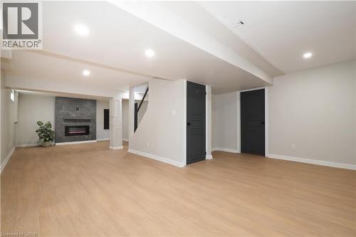 Spacious finished basement featuring wood-finish flooring, recessed lighting, and a modern electric fireplace with a dark stone-tile surround - 27 Scenic Wood Crescent, Kitchener, ON - Indoor With Fireplace