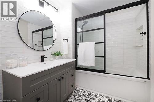 Bathroom featuring a gray vanity with an integrated sink, matte black fixtures, a round wall mirror, and a tub with sliding glass doors - 27 Scenic Wood Crescent, Kitchener, ON - Indoor Photo Showing Bathroom