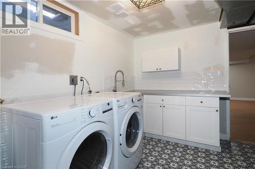 Laundry area with patterned tile flooring, shaker-style cabinetry, and a utility sink with a gooseneck faucet - 27 Scenic Wood Crescent, Kitchener, ON - Indoor Photo Showing Laundry Room