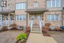 Brick townhouse exterior featuring multiple white-framed windows, a covered entrance with white railings, and a paver stone patio area - 275 Old Huron Road Unit# 21, Kitchener, ON  - Outdoor With Facade 