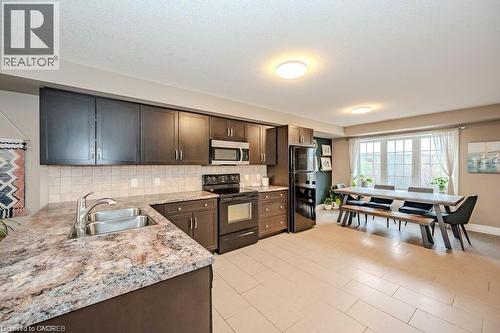 Spacious kitchen featuring dark wood cabinetry, a double basin stainless steel sink, and light-toned tile flooring - 275 Old Huron Road Unit# 21, Kitchener, ON - Indoor Photo Showing Kitchen With Double Sink
