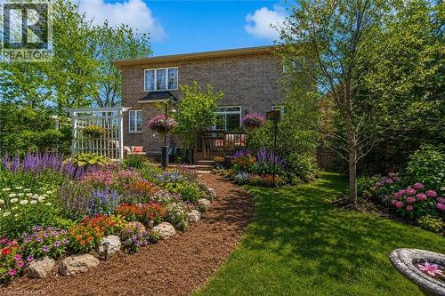 Landscaped backyard, mature trees, a wooden deck, and a brick exterior. (flowers are virtually staged) - 16 Westridge Drive, Hamilton, ON - Outdoor