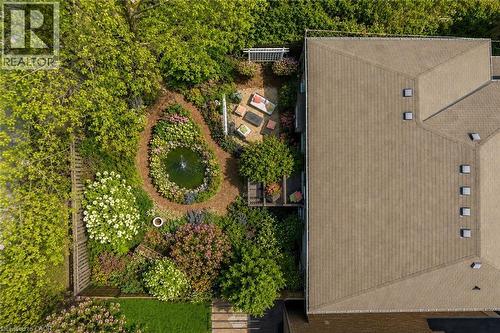 Landscaped backyard featuring  pond,  surrounding foliage, and a wood chip pathway, deck and a gravel patio area (flower and cushions are virtual staged) - 16 Westridge Drive, Hamilton, ON - Outdoor