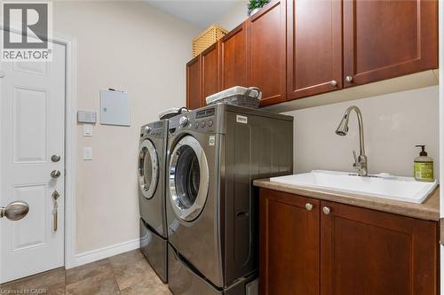 Main floor laundry room leads to a 2 car garage, sink with a gooseneck faucet, lots of cabinetry, tiled flooring - 16 Westridge Drive, Hamilton, ON - Indoor Photo Showing Laundry Room