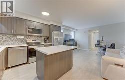 Contemporary kitchen featuring stainless steel appliances, grey wood-finish cabinetry, white countertops, and a mosaic tile backsplash - 