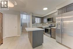 Kitchen with light wood-finish flooring, dark wood-finish cabinetry, stainless steel appliances, and a mosaic tile backsplash - 