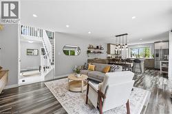 Open-concept living space featuring wood-finish flooring, recessed lighting, a modern kitchen with stainless steel appliances, a dining area with a linear pendant light fixture, and a staircase with w - 