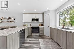 Modern kitchen featuring wood-finish flooring, two-tone cabinetry, stainless steel appliances, a large window, and recessed lighting - 